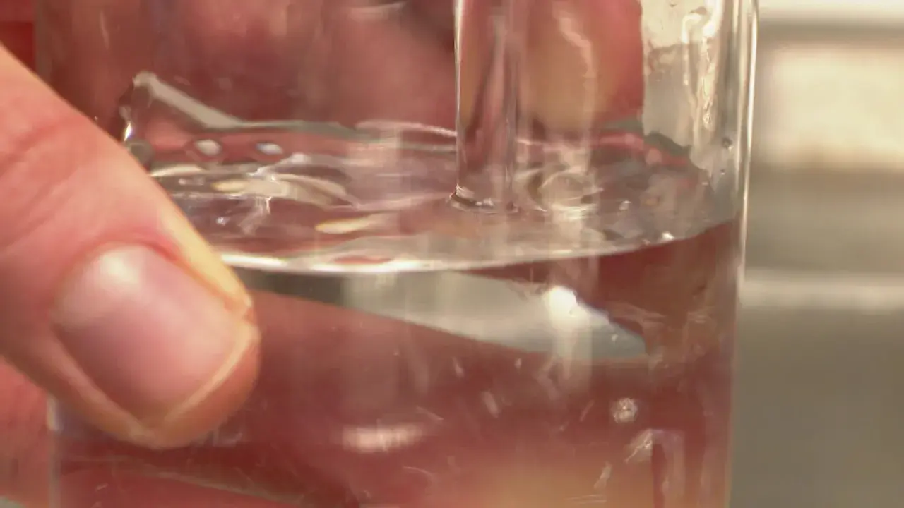 Main d'une personne tenant un verre d'eau potable à Poitiers. L'eau est claire et reflète la lumière.