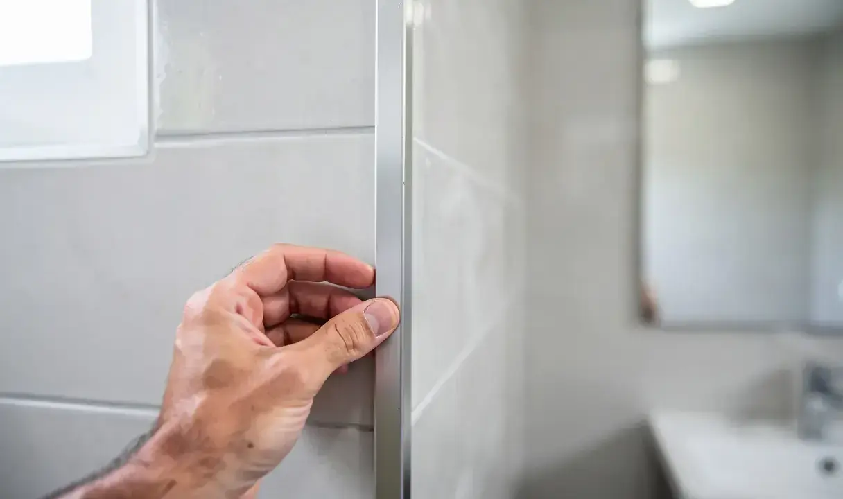 Main tenant vérifie le joint en L d'un profilé de finition sur un mur carrelé.