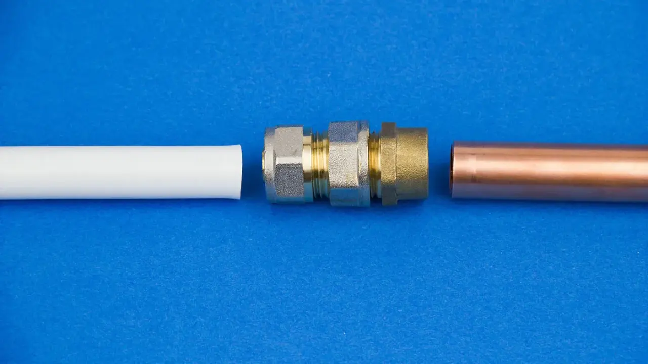 Raccordement de tuyaux : un coude 1/4 mâle femelle en laiton et un tube de cuivre à côté d'un tube blanc.