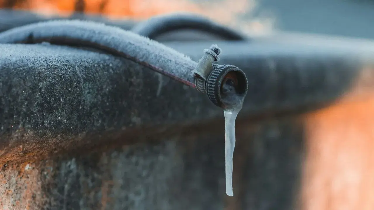 Un tuyau de jardin givré, avec une stalactite de glace tombant du robinet, illustre la nécessité de la protection tuyau en hiver.