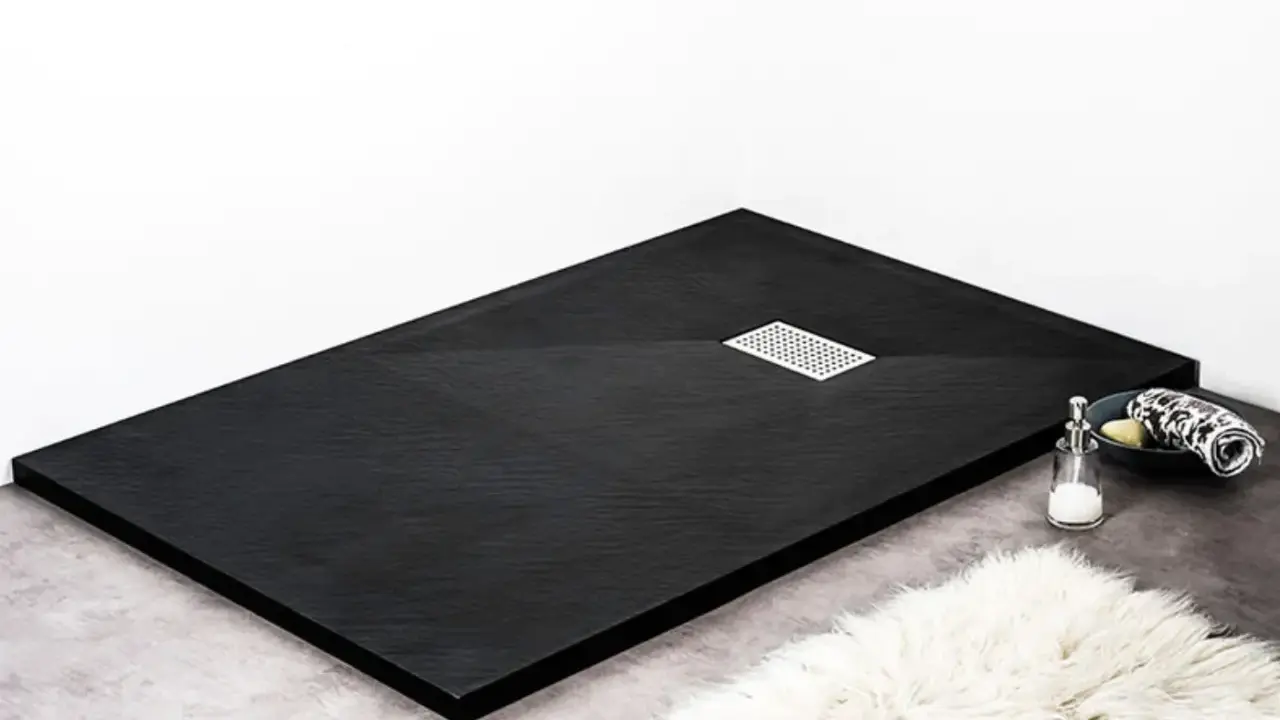 Receveur de douche noir texturé, avec une grille d'évacuation chromée. Un savon et une serviette sont posés sur le bord.