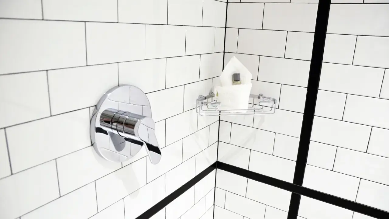 Un robinet de douche chromé et une étagère avec des serviettes sur un mur de carrelage blanc. Idéal pour nettoyer carrelage mural encrassé.