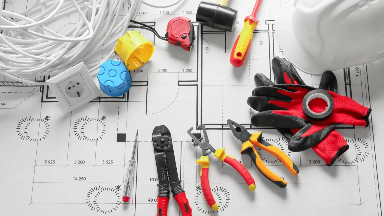 Outils d'électricien et rouleau de câble pour radiateur électrique, prêts pour l'installation sur un plan.
