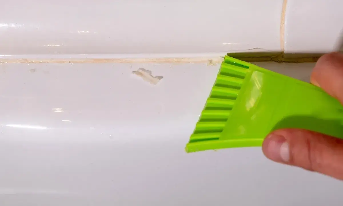 Outil vert raclant du mastic durci sur une surface blanche.