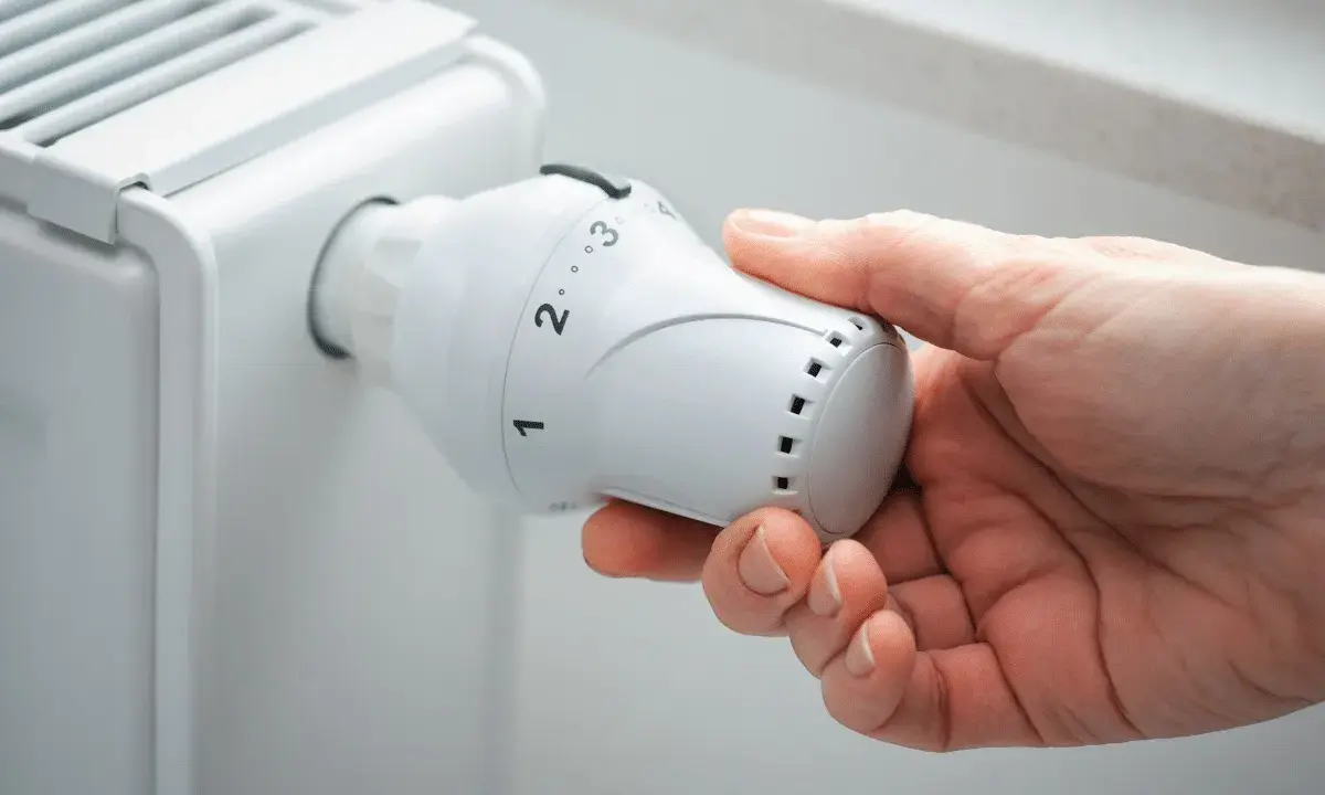 Main tenant ajuste le thermostat d'un radiateur, se demandant s'il faut fermer les radiateurs en été pour économiser de l'énergie.