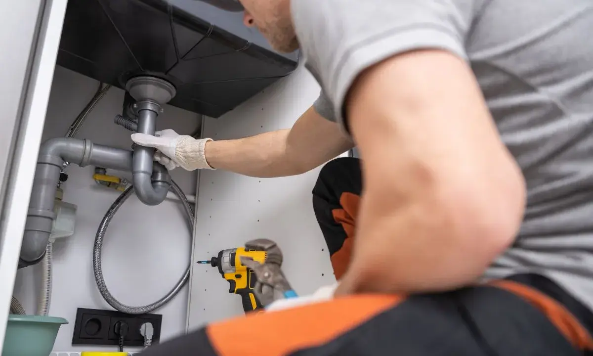 Plombier ajustant un siphon, utilisant une réduction excentrique pour un raccordement parfait sous l'évier.