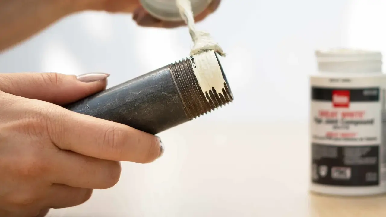 Application de pâte sur le filetage d'un **tube pour joint**. Un pot de pâte est visible à droite.