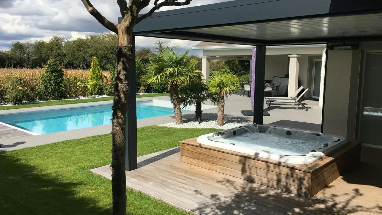 Un spa bouillonnant sur une terrasse en bois, à côté d'une piscine bleue. Le tableau temps de filtration piscine est visible dans le jardin luxuriant.