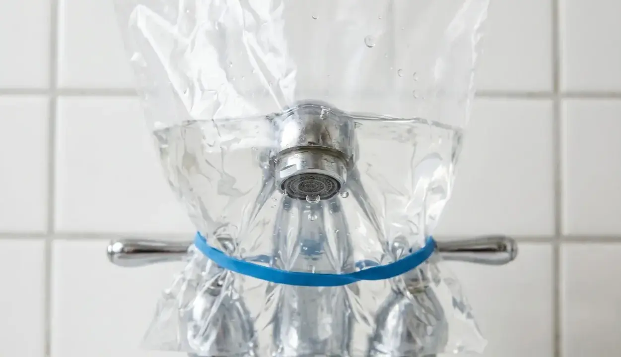 Un sac en plastique rempli d'eau est attaché à un robinet avec un élastique bleu. Une méthode pour enlever le calcaire de l'eau naturellement.