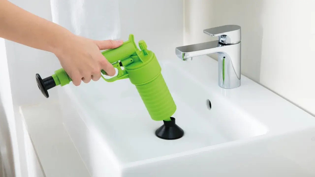 Main verte, un pistolet déboucheur est utilisé pour dégager un lavabo blanc.
