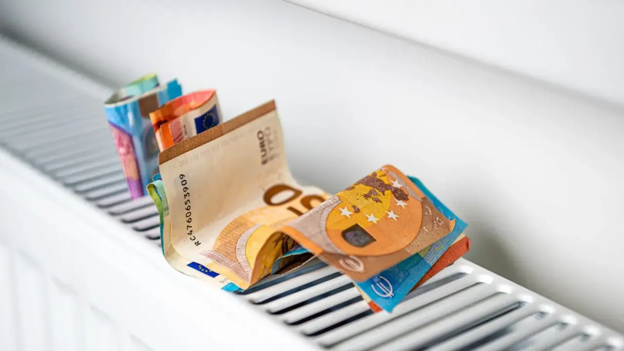Des billets en euros pliés sur un radiateur blanc, symbolisant le coût élevé du chauffage et la **consommation** du **radiateur hors gel**.