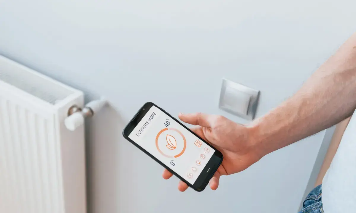Main d'un homme tenant un smartphone affichant l'application Netatmo pour contrôler un radiateur électrique en mode économie.