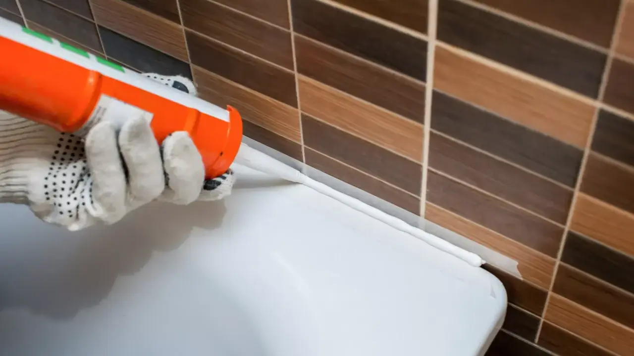 Application d'un joint silicone blanc à l'aide d'un pistolet, créant une barrière étanche entre le carrelage et une surface blanche.