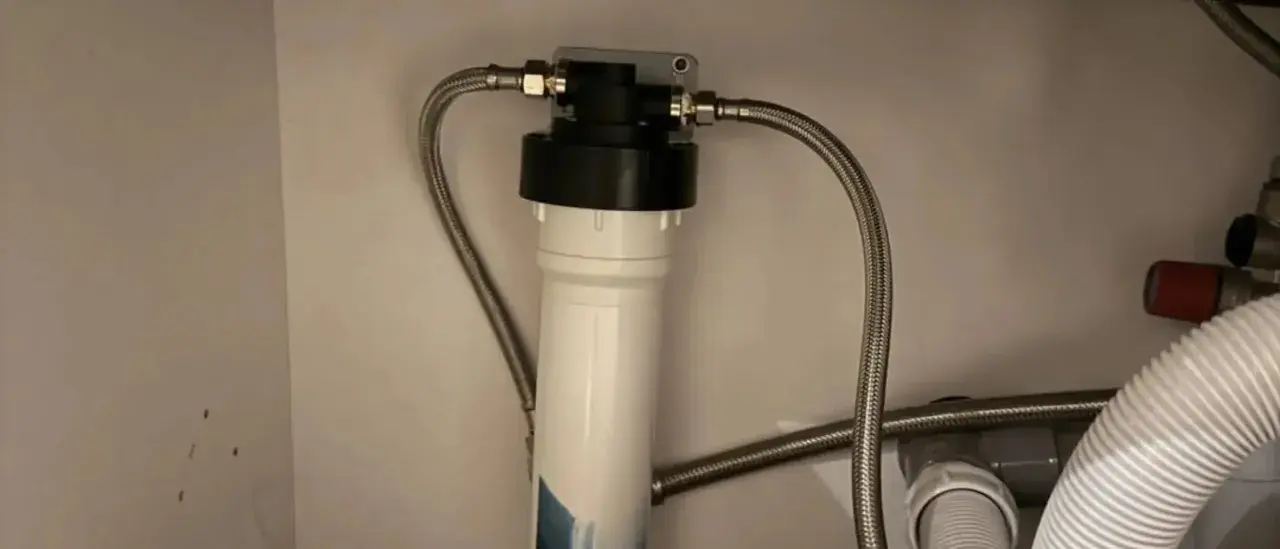 Système de filtration d'eau sous évier avec un cartouche charbon actif blanc et noir, relié par des tuyaux flexibles.