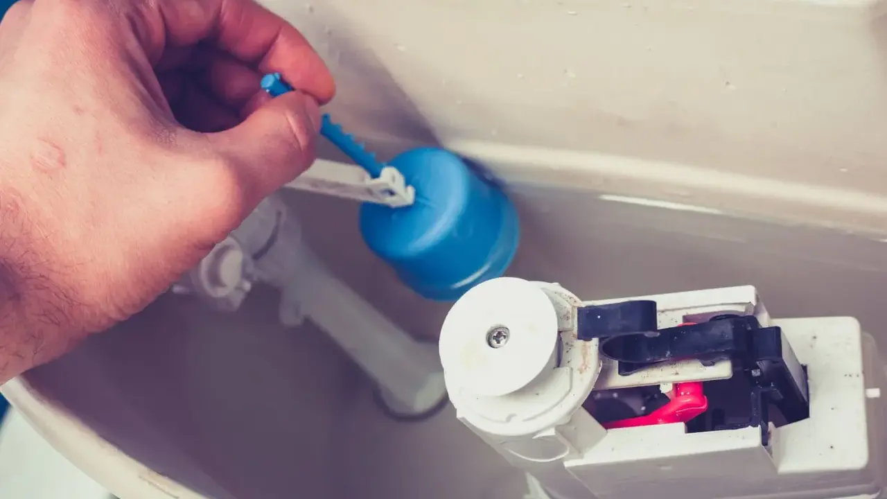 Main d'homme ajustant le flotteur bleu d'une chasse d'eau qui ne se remplit pas pour un wc suspendu.