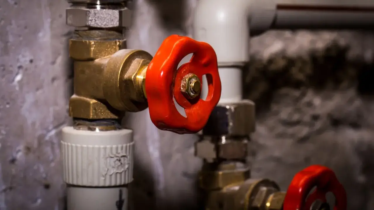 Gros plan sur un joint d'électrovanne avec une poignée rouge vif, faisant partie d'un système de plomberie complexe.