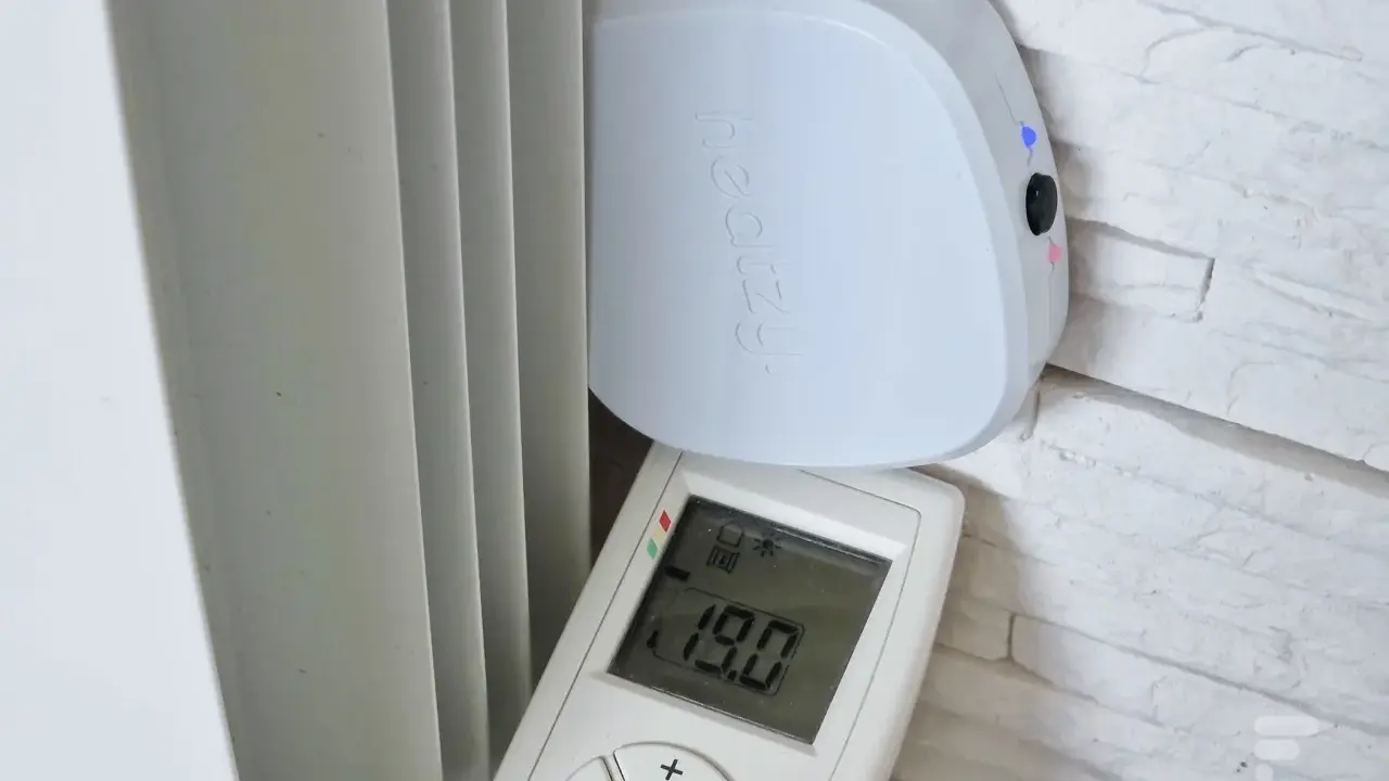 Schéma branchement thermostat chauffage électrique : un boîtier blanc "heatzy" et une télécommande affichant 19.0°C, près d'un radiateur.