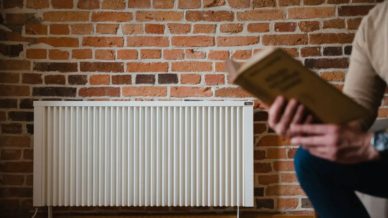 Un homme lit un livre près d'un radiateur blanc. La question quelle puissance de radiateur pour 25 m2 est au cœur de ce décor cosy.