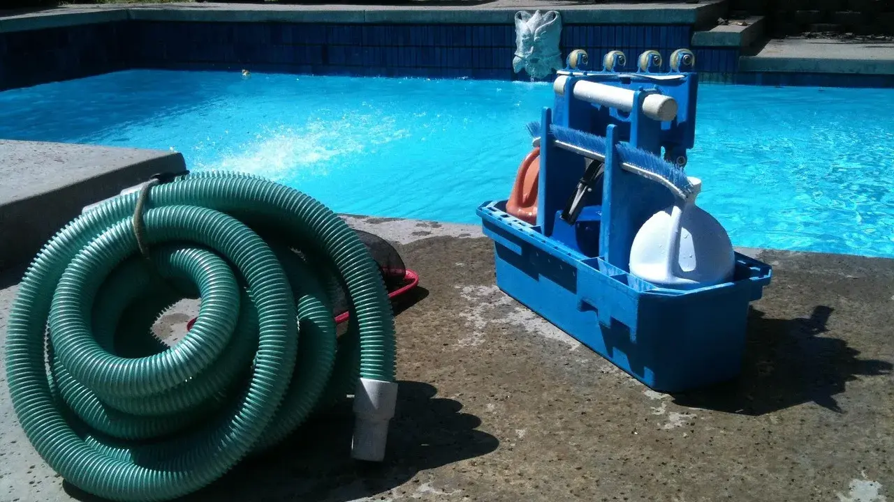 Un tuyau vert enroulé et une boîte bleue avec des accessoires de piscine, prêts pour le nettoyage. L'ordre des filtres à eau est essentiel pour une eau claire.