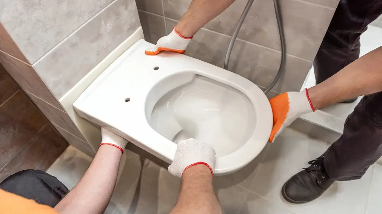 Mains gantées installent un WC suspendu. L'opération est délicate, mais le résultat sera moderne et pratique.