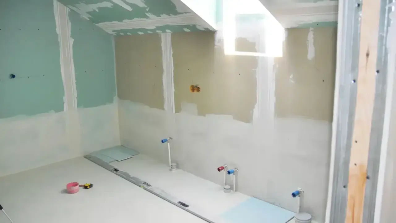 Travaux de finition dans une salle de bain : murs en plaques de plâtre, arrivées d'eau et niveau à bulle au sol. Isolation salle de bain en cours.