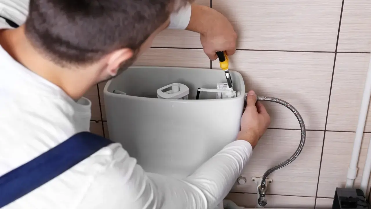 Un plombier répare une chasse d'eau qui coule. Il utilise une pince pour ajuster le mécanisme interne du réservoir.