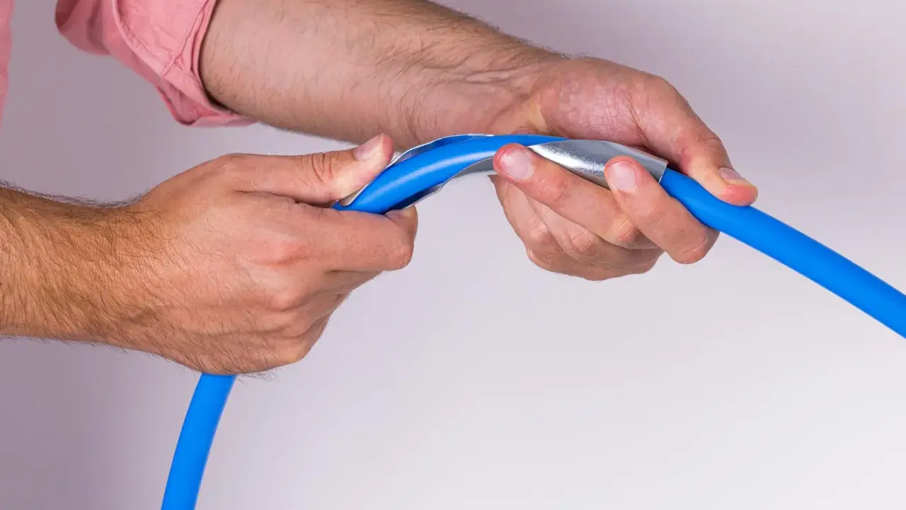Mains bleues tenant un tuyau bleu avec un outil métallique pour former un coude boule.