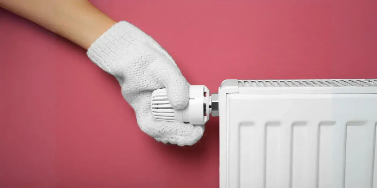 Main tenant, avec un gant blanc, ajuste le thermostat d'un radiateur pour choisir entre le chauffage mode eco ou confort.
