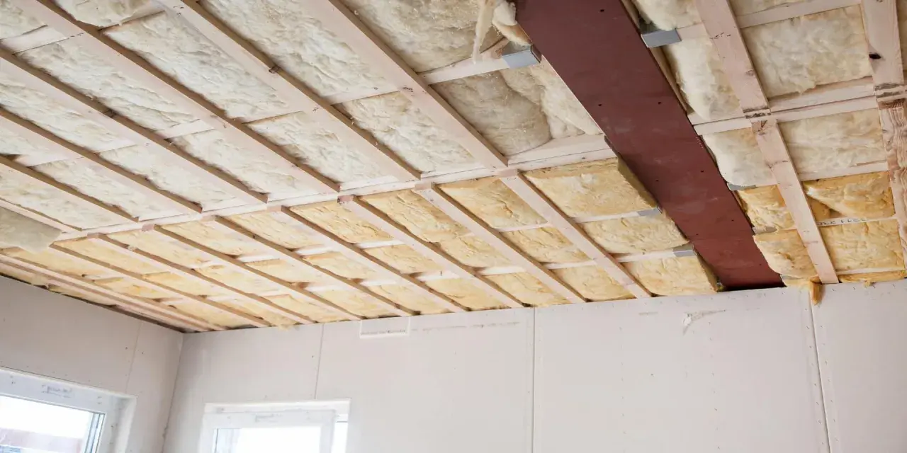 Isolation thermique plafond en cours d'installation, avec des panneaux de laine minérale entre les solives en bois.