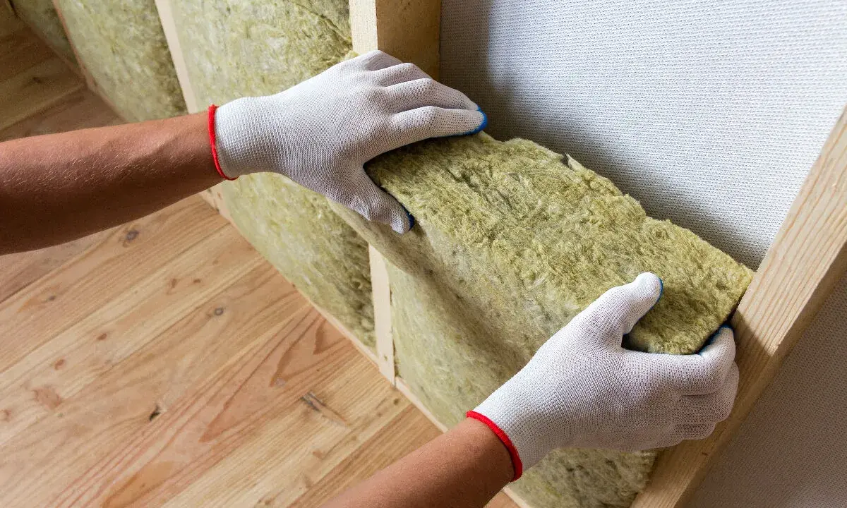 Mains gantées insèrent un isolant dans une structure en bois pour isoler sa maison.