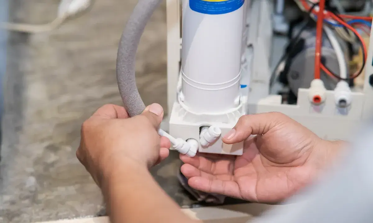 Mains d'un technicien connectant un tuyau à un système de filtration d'eau, peut-être pour résoudre un problème où le sel de mon adoucisseur ne fond pas.