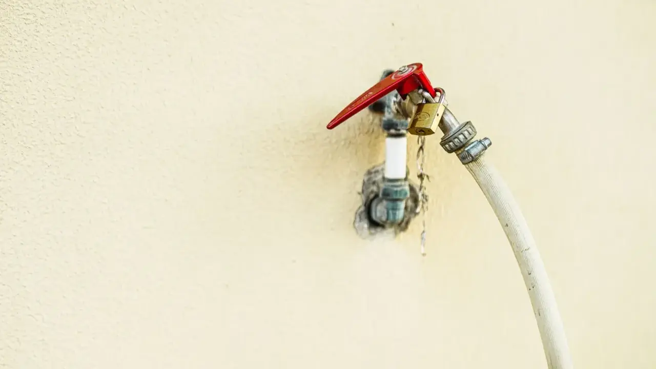 Robinet extérieur avec un cadenas doré et un tuyau blanc, le raccord asymétrique suggère une utilisation inhabituelle.