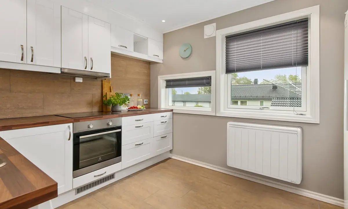 Cuisine moderne avec placards blancs, plan de travail en bois et un radiateur blanc discret assurant le chauffage.