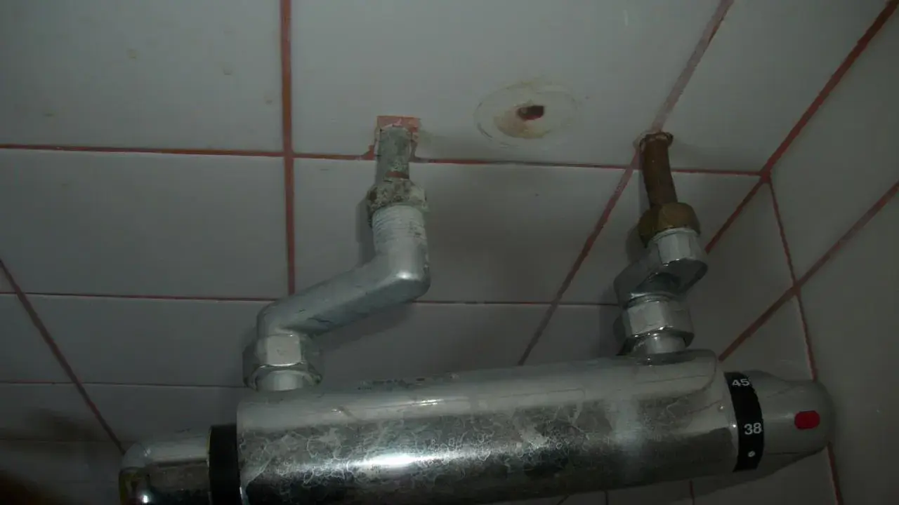 Un excentrique robinet de douche, fixé au mur carrelé, avec des tuyaux argentés et des indications de température.