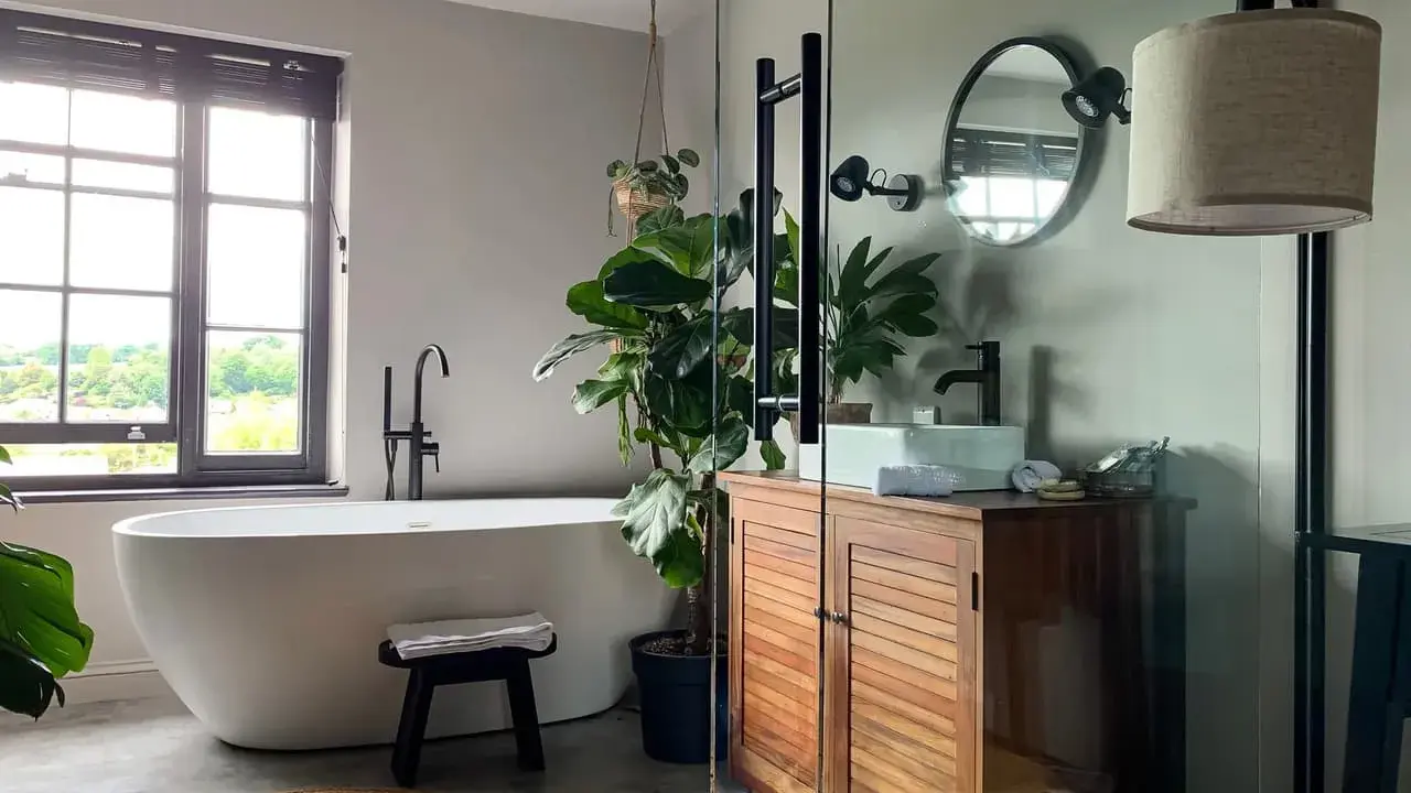 Une salle de bain moderne et épurée, parfaite pour refaire salle de bain. Baignoire îlot, meuble en bois, plantes vertes et lumière naturelle.