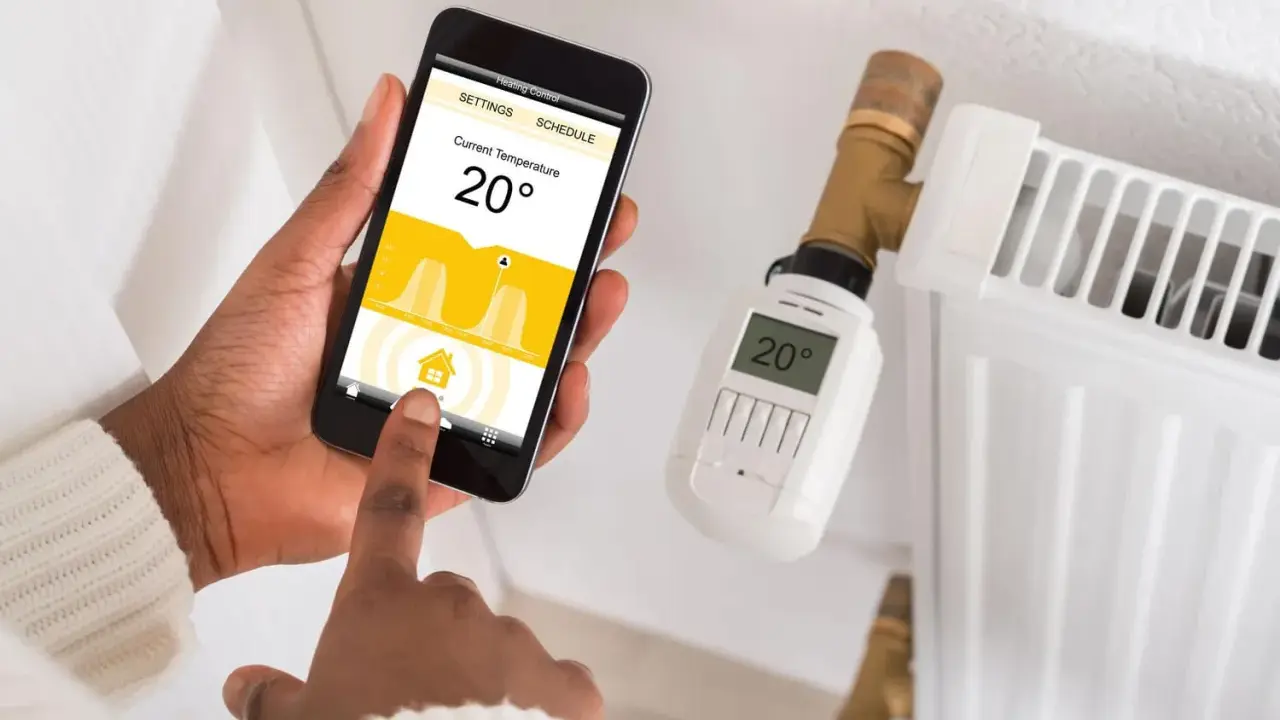 Maintenant, contrôlez votre chauffage à distance avec des solutions domotiques. Une main utilise un smartphone pour régler la température d'un radiateur.
