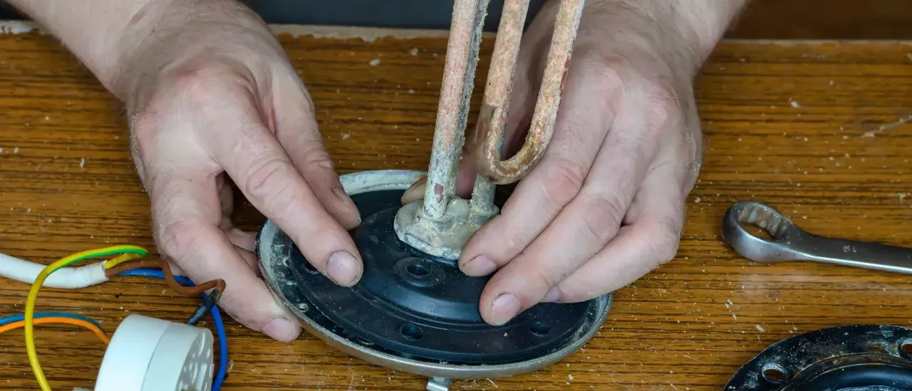 Mains de l'homme ajustant un élément chauffant entartré sur un joint plat, prêt pour le remplacement.