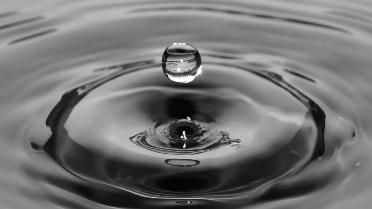 Goutte d'eau en suspension au-dessus de son impact, créant des ondulations. L'eau calcaire reflète la lumière.