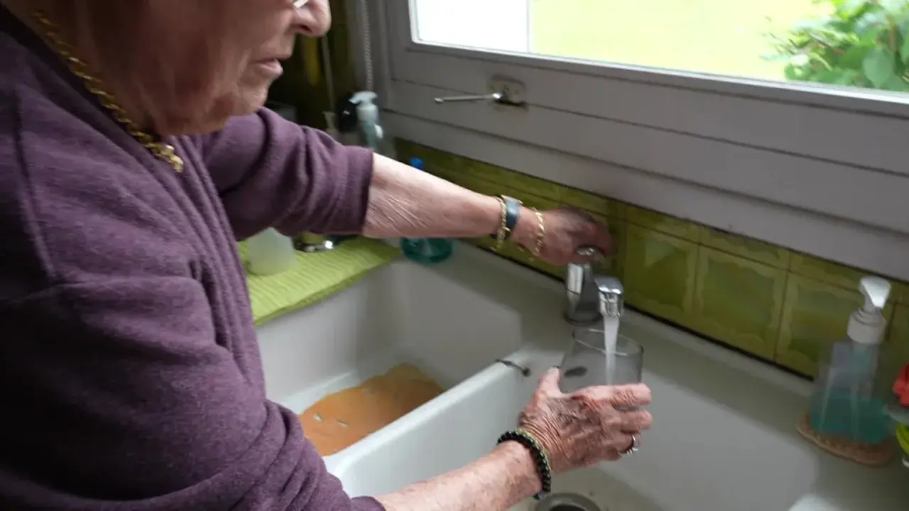 Une femme remplit un verre d'eau du robinet. L'eau de Beauvais coule fraîchement.