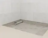 Installation d'un receveur de douche : un siphon est posé sur une chape avant le carrelage.
