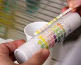 Bandelette réactive pour la mesure de dureté de l'eau, comparée à un tableau de couleurs.