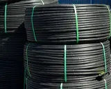 Rouleaux de tube plastique flexible noir, attachés par des sangles vertes, prêts pour l'irrigation.