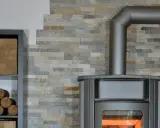 Poêle à bois moderne avec conduit métallique, prêt à réchauffer la pièce. Des bûches sont stockées sur une étagère à côté.