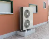 Unité extérieure de pompe à chaleur, avec ses deux ventilateurs, installée sur un socle devant un mur ocre. Le poids de cet appareil assure sa stabilité.