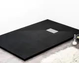 Receveur de douche noir texturé, avec une grille d'évacuation chromée. Un savon et une serviette sont posés sur le bord.