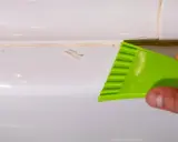 Outil vert raclant du mastic durci sur une surface blanche.