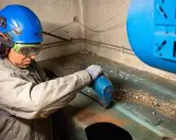 Un ouvrier en casque bleu et lunettes effectue l'inertage d'une cuve, utilisant un outil pour nettoyer la surface.