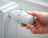 Main tenant ajuste le thermostat d'un radiateur, se demandant s'il faut fermer les radiateurs en été pour économiser de l'énergie.