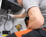 Plombier ajustant un siphon, utilisant une réduction excentrique pour un raccordement parfait sous l'évier.