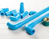 Ensemble de tuyaux et raccords bleus en PVC, prêts pour une installation. Un pot de colle est à proximité.